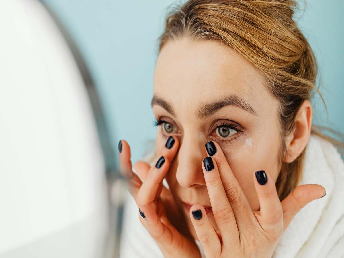 donna davanti allo specchio che si dà la crema in faccia